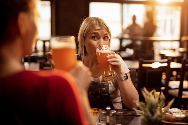 Молодая женщина и ее подруга пьют пиво и наслаждаются обедом в ресторане