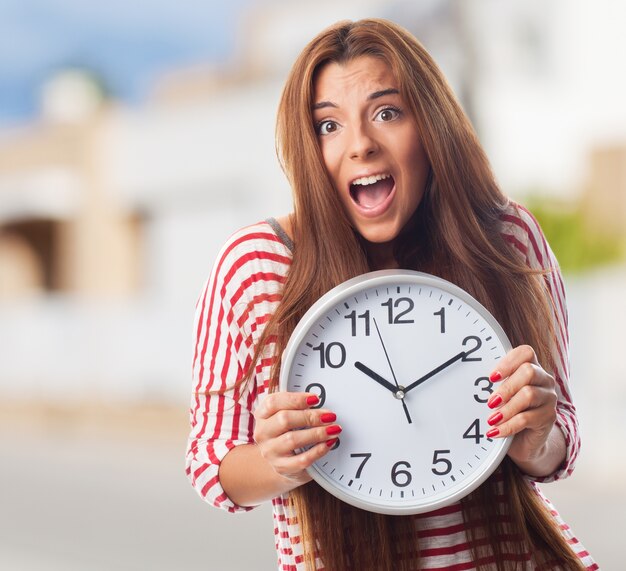 Young woman hiding behind round wall clock. 