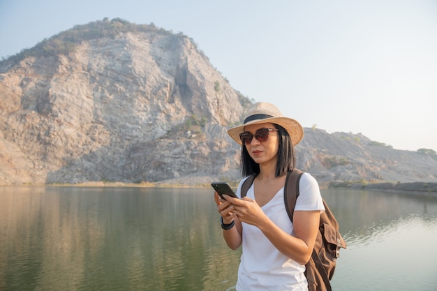 若い女性のハイカーは山で写真を撮るスマートフォンを使用します