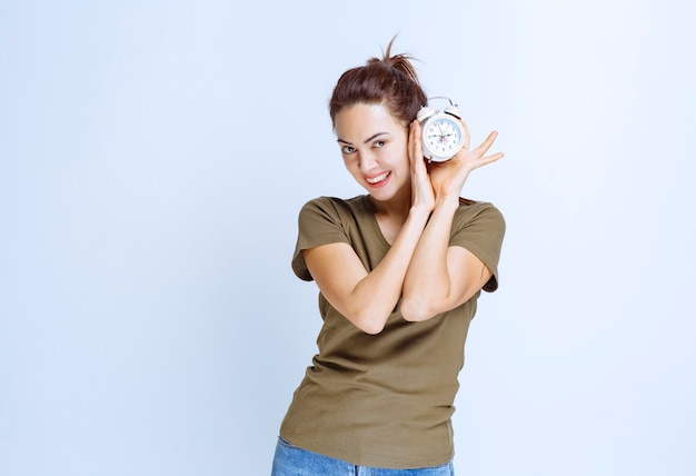 Free photo young woman holding an alarm clock and looks satisfied as she is never late