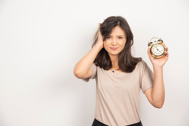 Young woman holding alarm clock on white background.