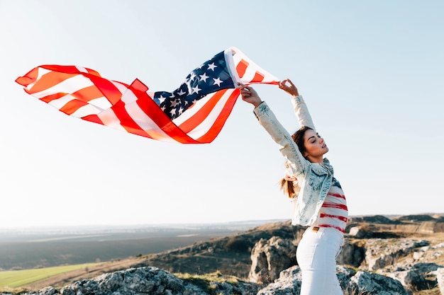 Молодая женщина держит американский флаг на вершине горы