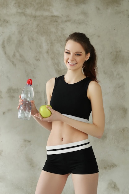Молодая женщина, держащая яблоко и бутылку с водой