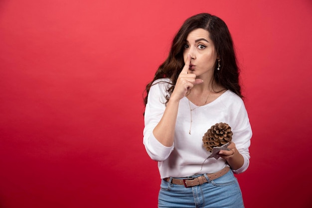 Young woman holding a big Christmas pinecone and giving silence sign. High quality photo