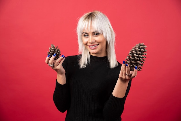 Young woman holding big pinecones on a red wall. 