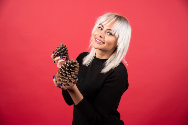 Free photo young woman holding big pinecones on a red wall.