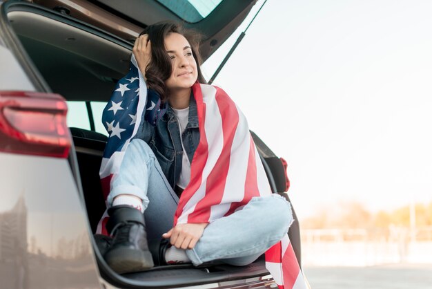 Young woman holding big usa flag in car trunk