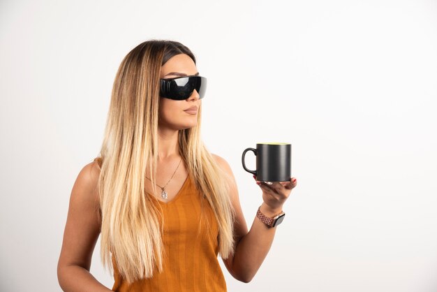 Young woman holding black cup and wearing goggles.