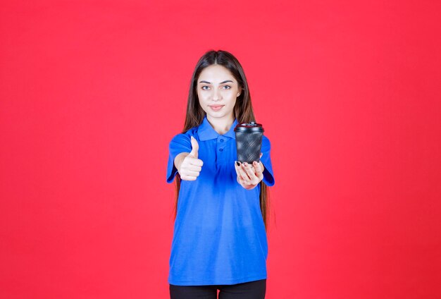 Young woman holding a black disposable coffee cup and showing positive hand sign