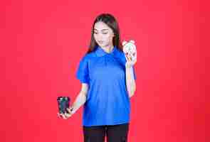 Free photo young woman holding a black disposable cup of drink and an alarm clock