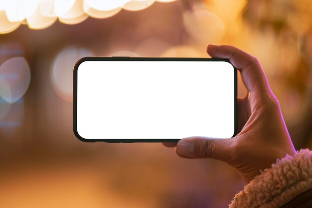 Young woman holding a blank smartphone with bokeh effect around