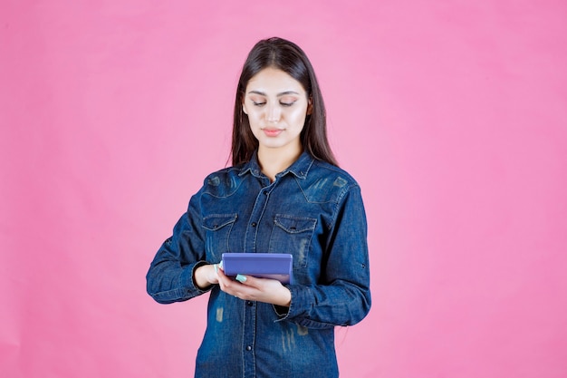 Молодая женщина держит в руке синий калькулятор и вычисляет