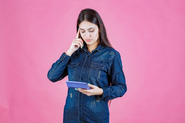 Young woman holding a blue calculator and thinking