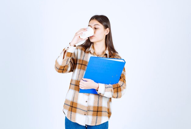 Young woman holding blue folder and drinking cup of coffee. 
