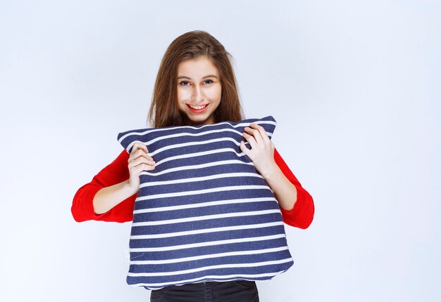 young woman holding a blue striped pillow and feeling positive.