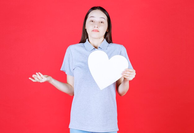 Young woman holding board in a heart shape and doesn't know what to do