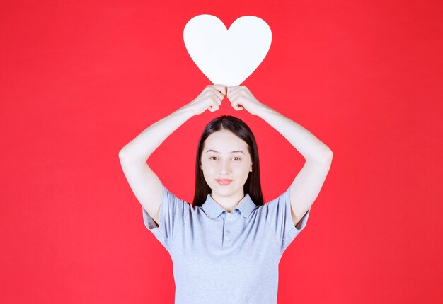 Young woman holding board in a heart shape top of her head