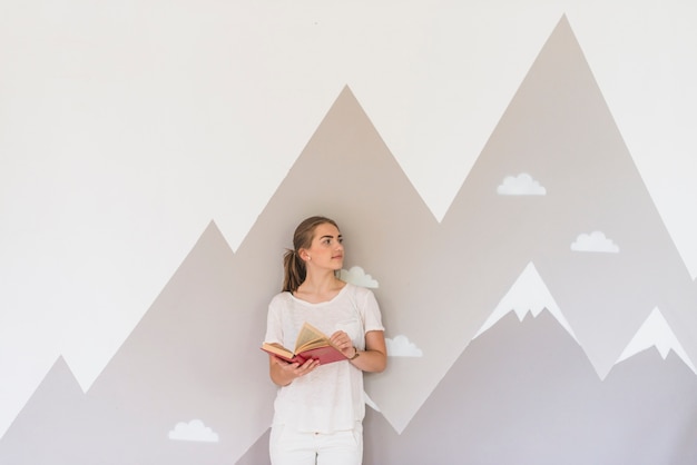 Young woman holding book standing against graffiti wall