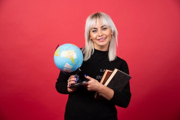 Young woman holding books with earth globe and smiling