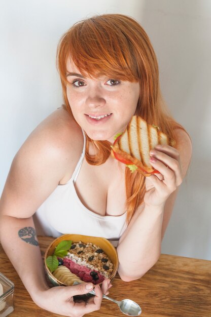 Молодая женщина с миской из овсяной муки и сэндвич с грилем