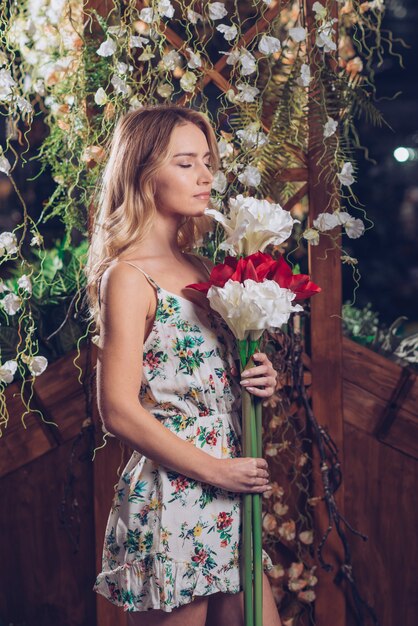 Young woman holding bunch of artificial white and red flowers standing in garden