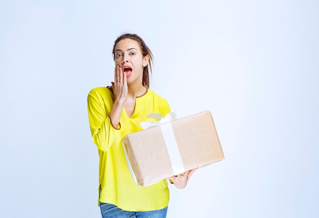 Free photo young woman holding a cardboard gift box and thinking about the unknown sender