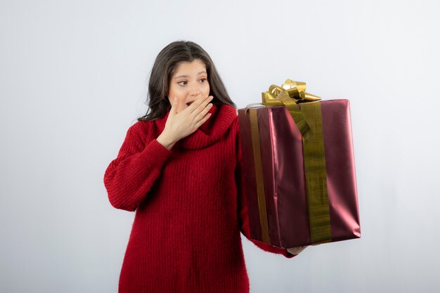 Young woman holding Christmas gift over white wall. 
