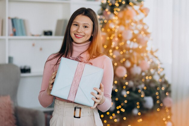 クリスマスツリーがクリスマスプレゼントを保持している若い女性