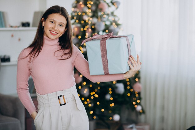 Young woman holding christmas present by christmas tree