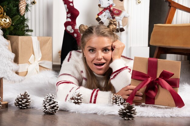 A young woman holding a Christmas present and lying down on carpet.