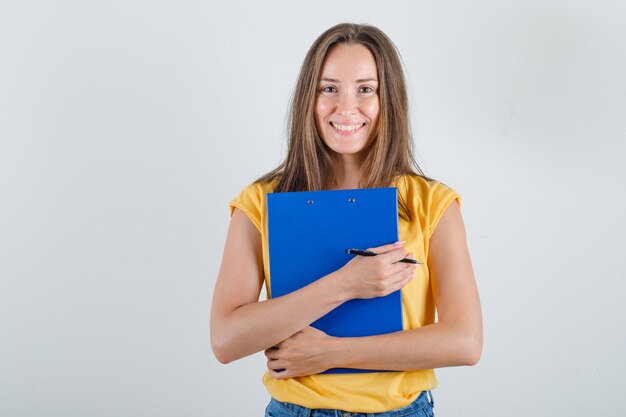 Young woman holding clipboard and pen in t-shirt, shorts and looking cheerful