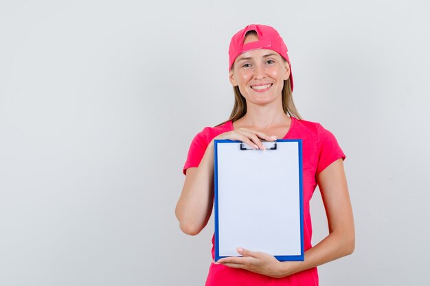 Молодая женщина, держащая буфер обмена в розовой футболке, кепке и веселый вид, вид спереди.