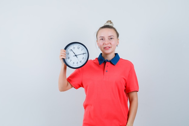 Young woman holding clock in t-shirt and looking cheery