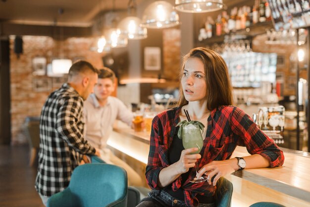 Молодая женщина, держащая коктейльное стекло в баре