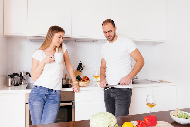 Young woman holding coffee cup in hand looking at her husband sharpening the knife