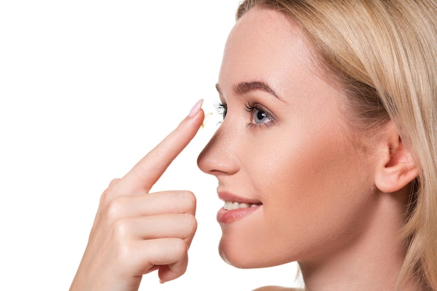 Young woman holding contact lens on index finger with copy space. Close up face of healthy beautiful woman about to wear contact lens. Eyesight and ophthalmology concept.