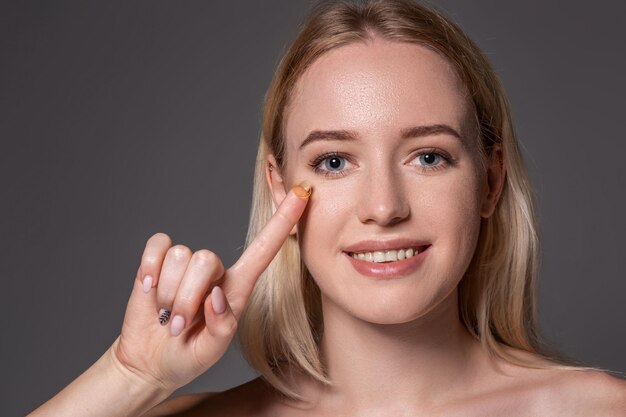 Young woman holding contact lens on index finger with copy space. Close up face of healthy beautiful woman about to wear contact lens. Eyesight and ophthalmology concept.