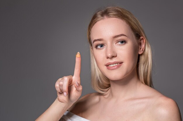 Young woman holding contact lens on index finger with copy space. Close up face of healthy beautiful woman about to wear contact lens. Eyesight and ophthalmology concept.
