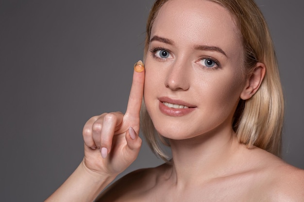 Young woman holding contact lens on index finger with copy space. Close up face of healthy beautiful woman about to wear contact lens. Eyesight and ophthalmology concept.