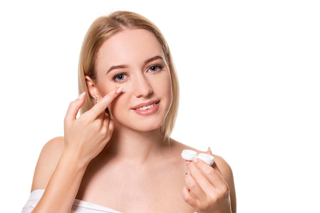 Young woman holding contact lenses cases and lens in front of her face on white background. Eyesight and ophthalmology concept.