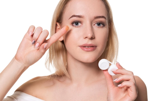 Young woman holding contact lenses cases and lens in front of her face on white background. Eyesight and ophthalmology concept.