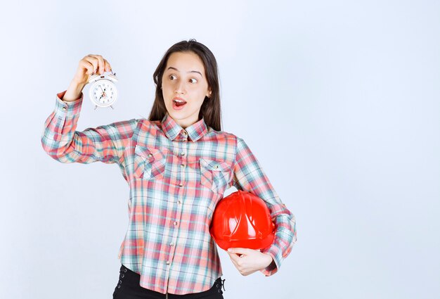 A young woman holding crash helmet and an alarm clock .
