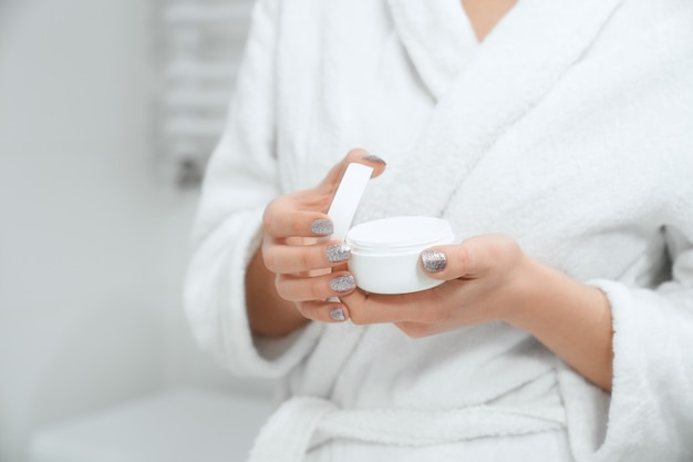 Young woman holding cream for body or face in bathroom