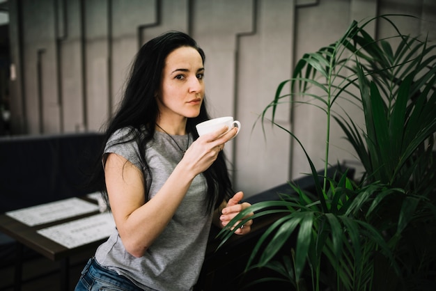 Young woman holding cup of drink near table and sofas