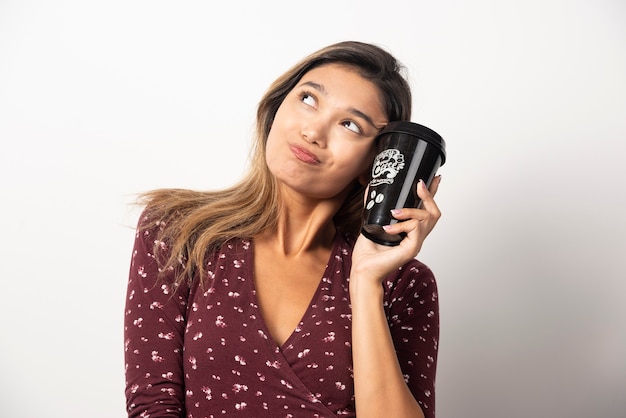 Young woman holding a cup of drink on white wall. 