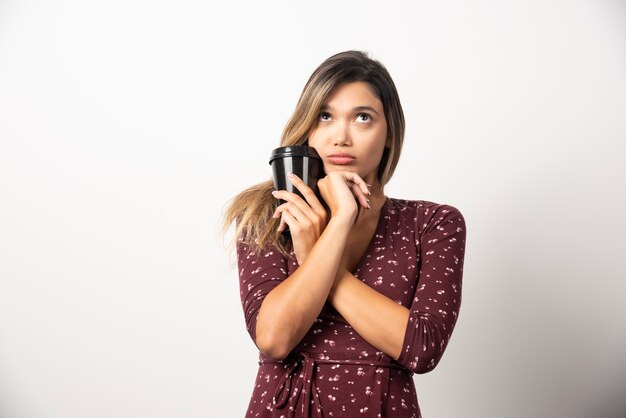 Young woman holding a cup of drink on white wall. 