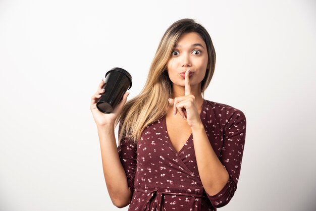 Young woman holding a cup of drink on white wall. 