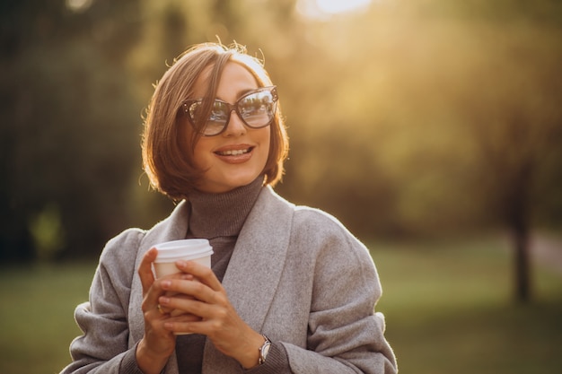 公園で暖かいコーヒーのカップを保持している若い女性