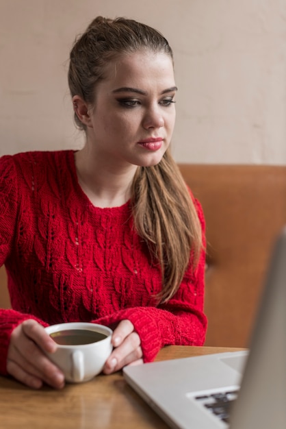 彼女のラップトップを見ながら若い女性がカップを保持しています