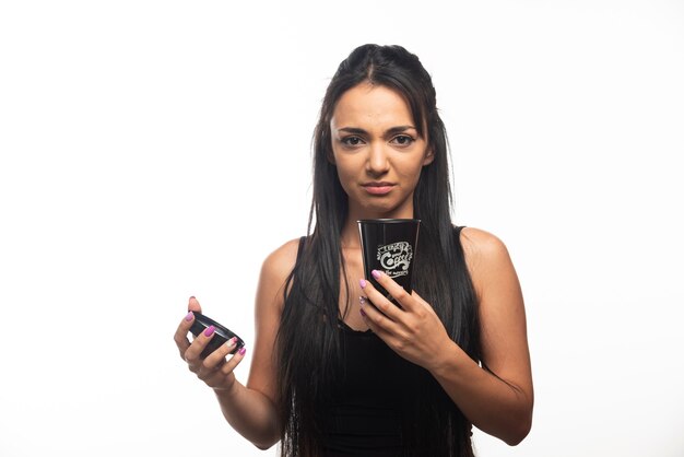 Young woman holding a cup on white wall